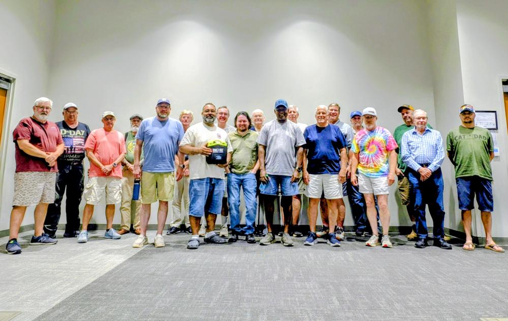 Group of men standing indoors, some smiling, wearing casual clothing.