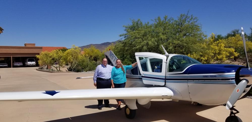 Man and woman standing next to a small airplane on a sunny day.