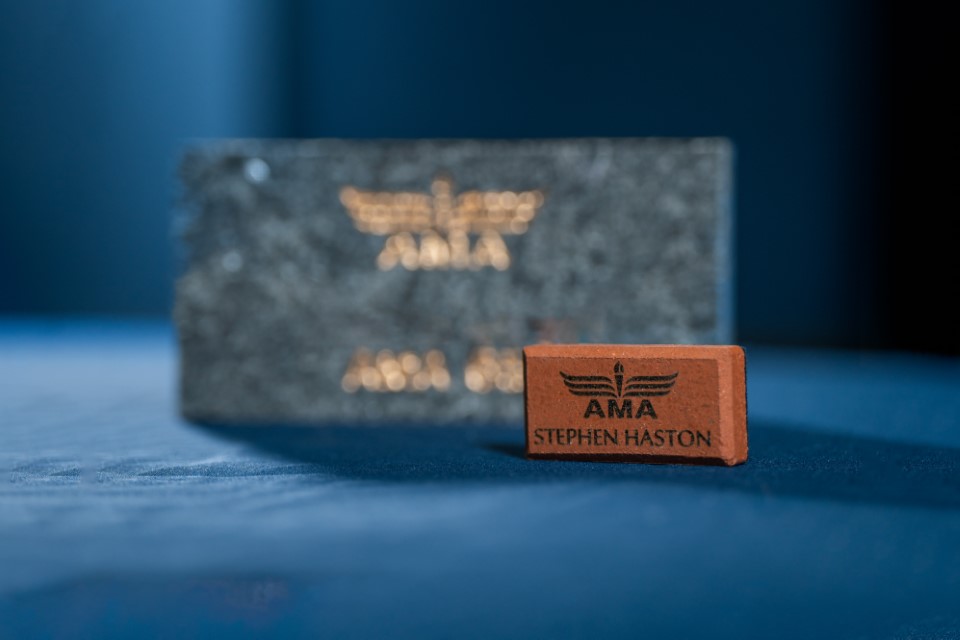 Black and red AMA logos on stone and brick blocks, blue background.