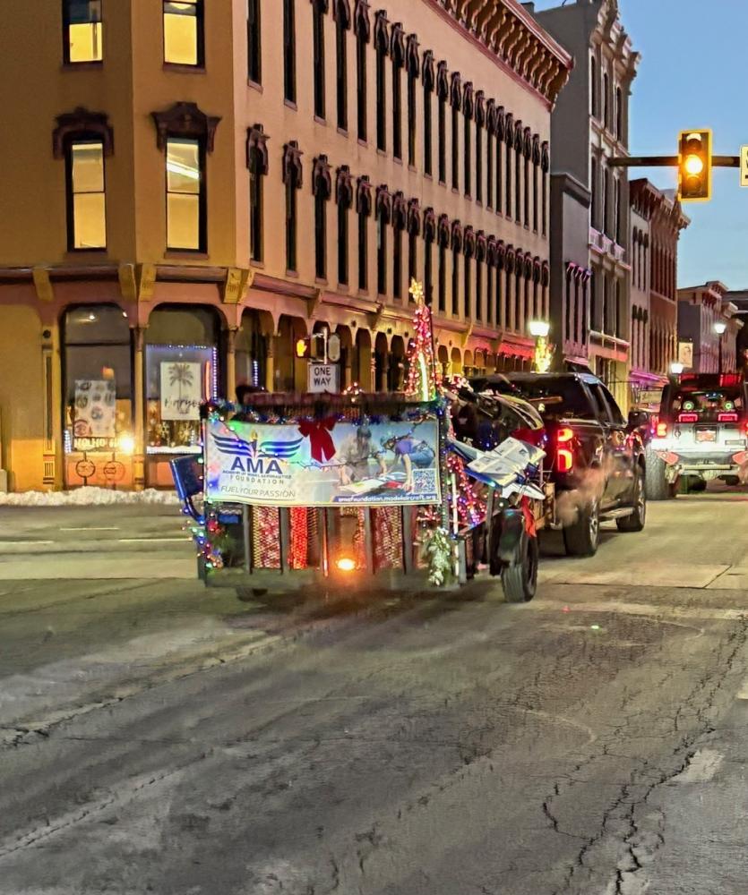 A festively decorated truck with lights, moving through a city street at dusk.