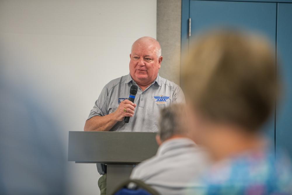 Man speaking at podium with microphone, wearing a grey shirt.