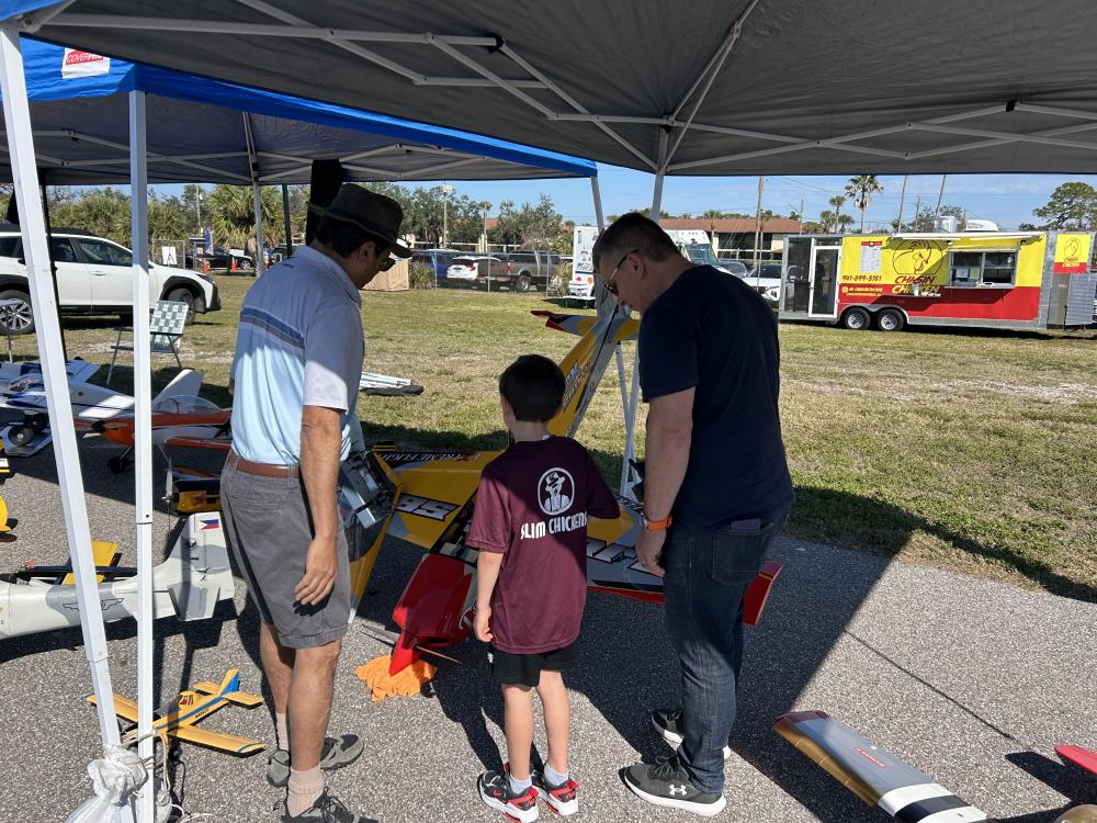 Three people examining model aircraft at an outdoor event.