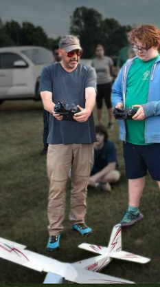 Two people flying remote-controlled planes in a grassy field.