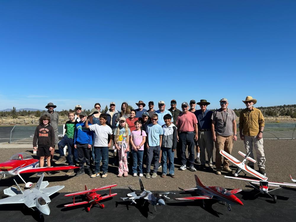 A group of people outdoors with model airplanes on the ground.