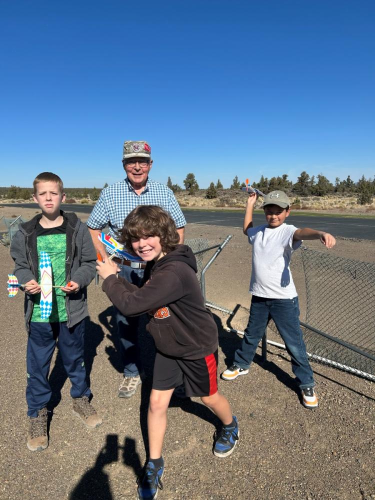 Four people smiling outdoors near a chain-link fence.
