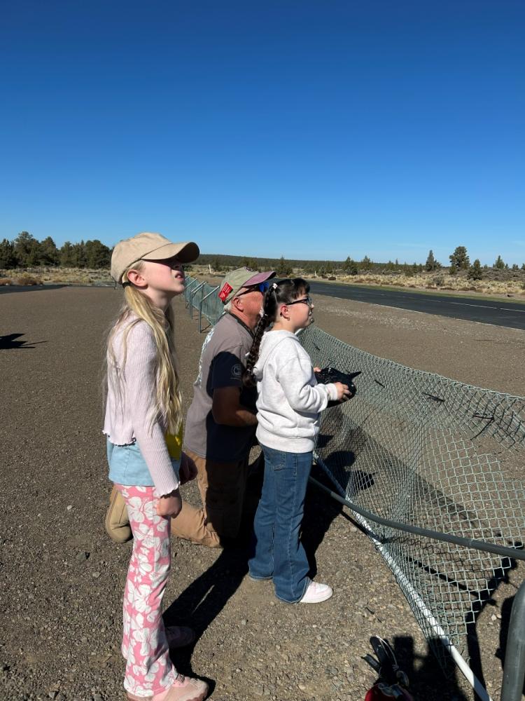 Three people standing near a netted fence under a clear blue sky.