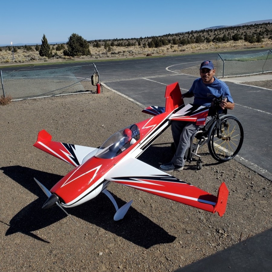 Man in a wheelchair beside a large red and white model plane on a tarmac.