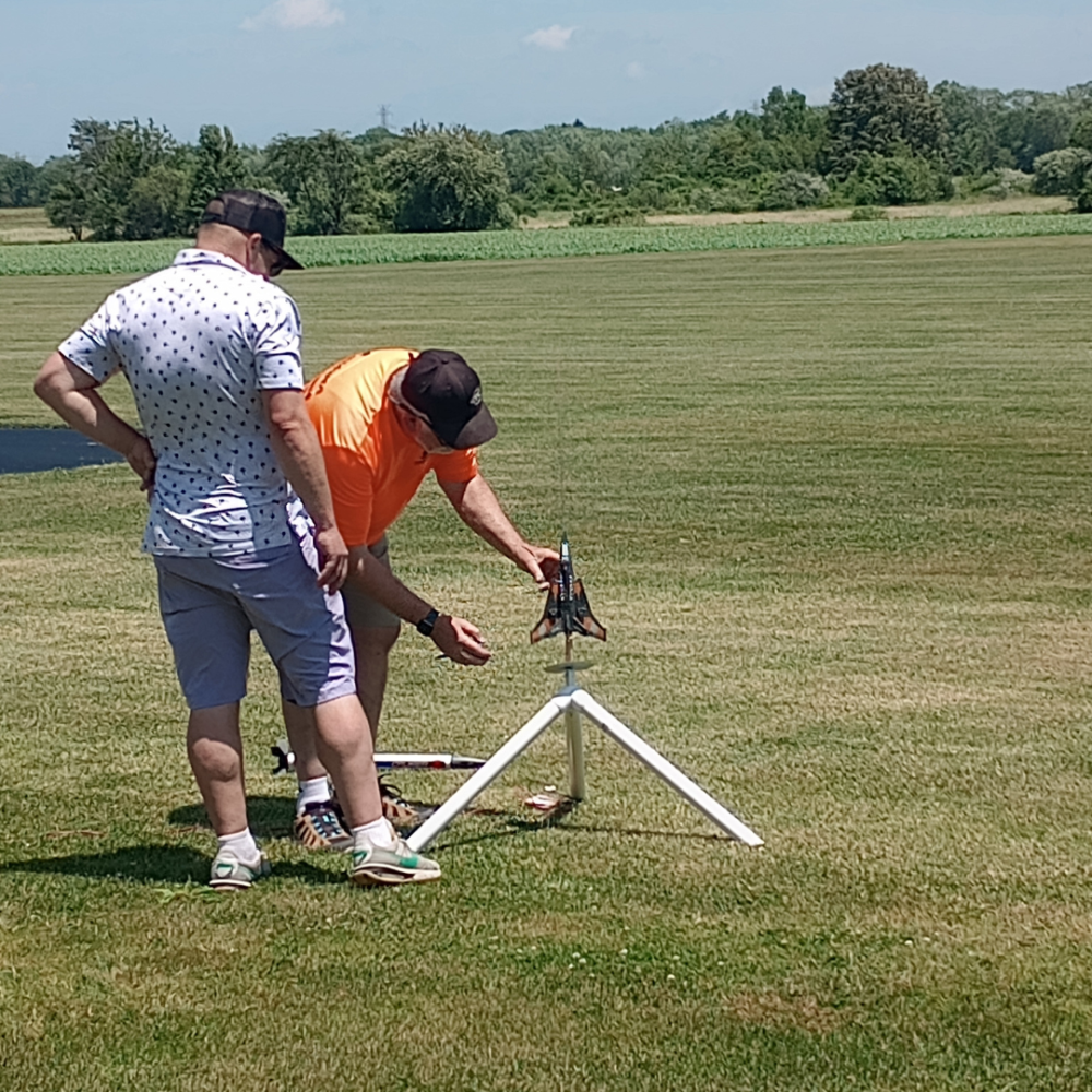 Two men setting up a model rocket on a grassy field.
