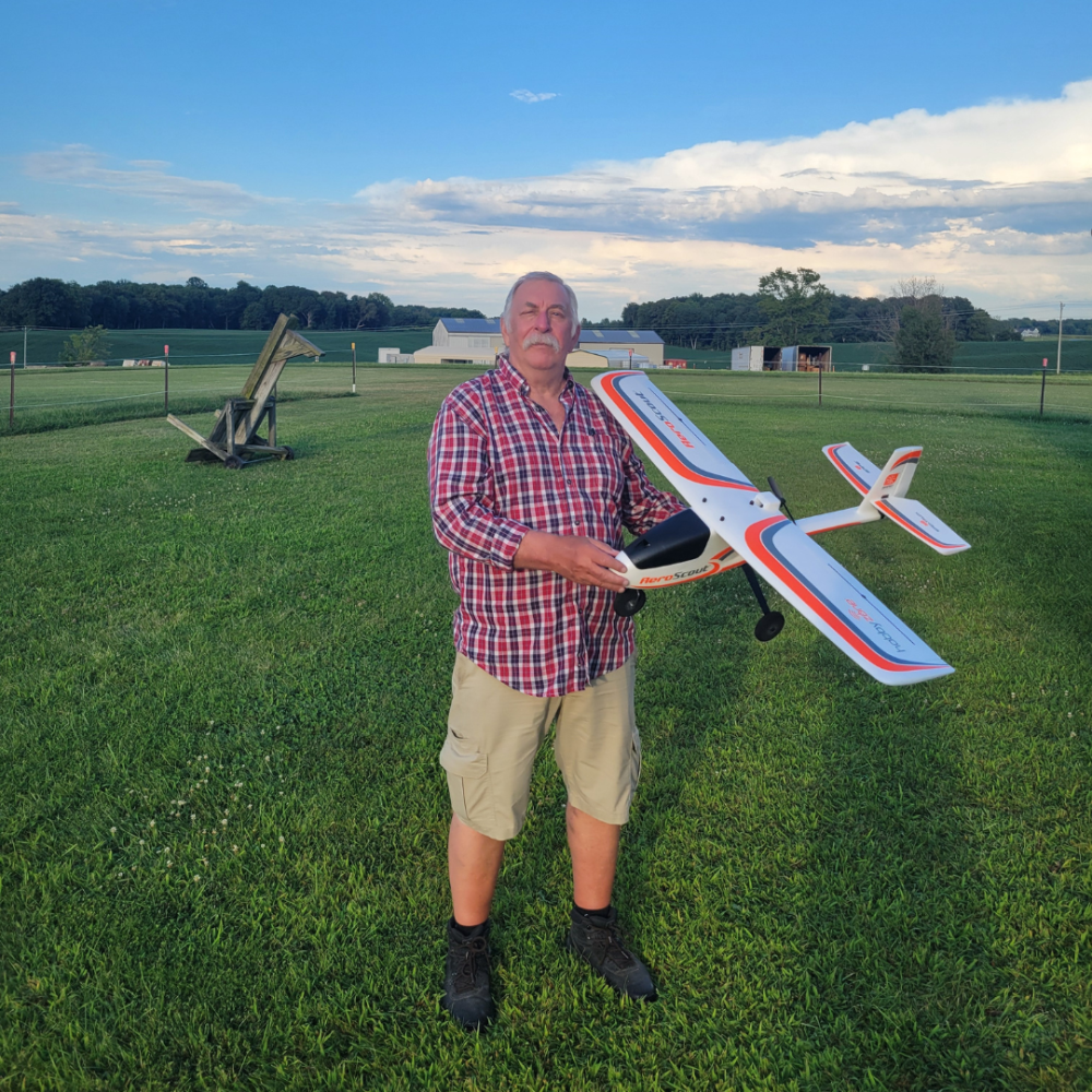 Man holding a model airplane on a grassy field at sunset.