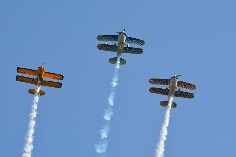Three biplanes with smoke trails against a clear blue sky.