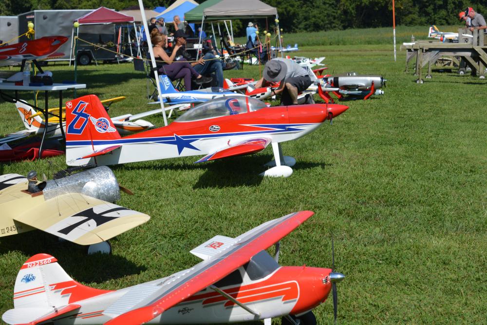 Model airplanes displayed on grass with people adjusting them under tents.