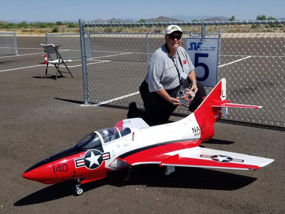 Person with a large remote-controlled jet model on an airstrip.