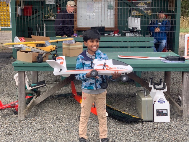 Young boy smiling, holding a model airplane in an outdoor setting.