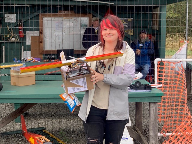 Person holding a colorful model airplane in front of a clubhouse display.