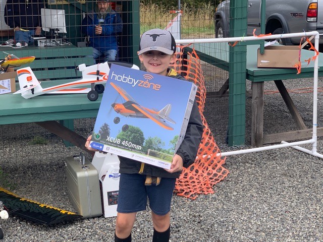 Child holding a model airplane box at an outdoor hobby event.