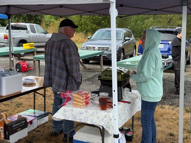 Outdoor gathering under canopy, two people talking near a table with food items.