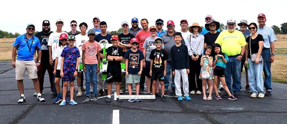 Group of people of various ages smiling outdoors on a paved surface.