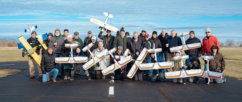 Group of people holding model airplanes on a runway.