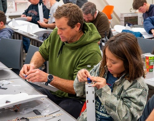 Man and child assembling parts in a classroom.