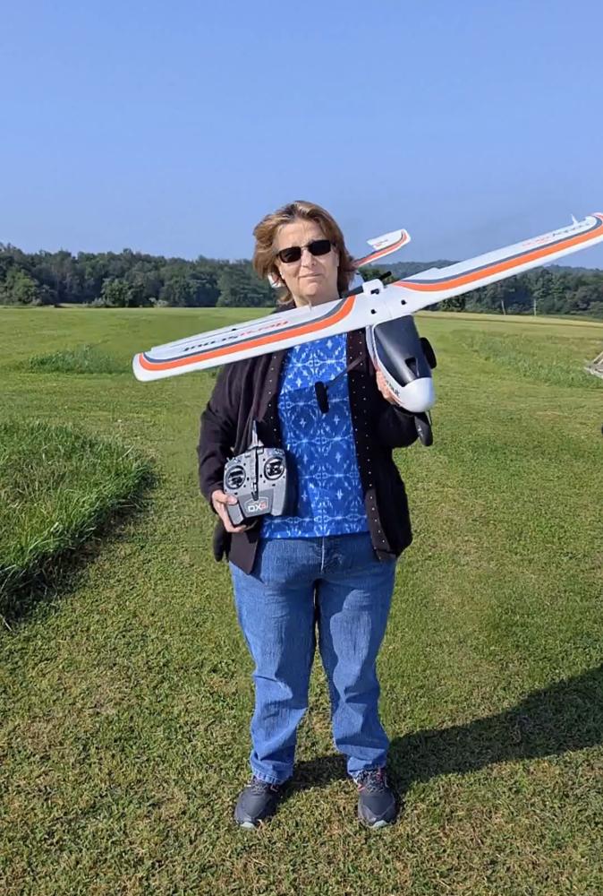 Woman holding a model plane and remote control on a grassy field.