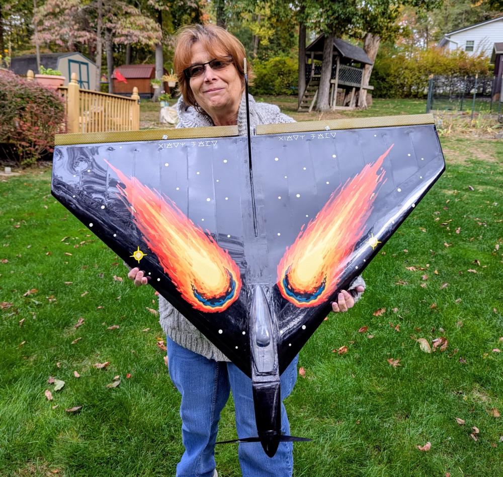 Person holding triangular model with flaming comet design outdoors.