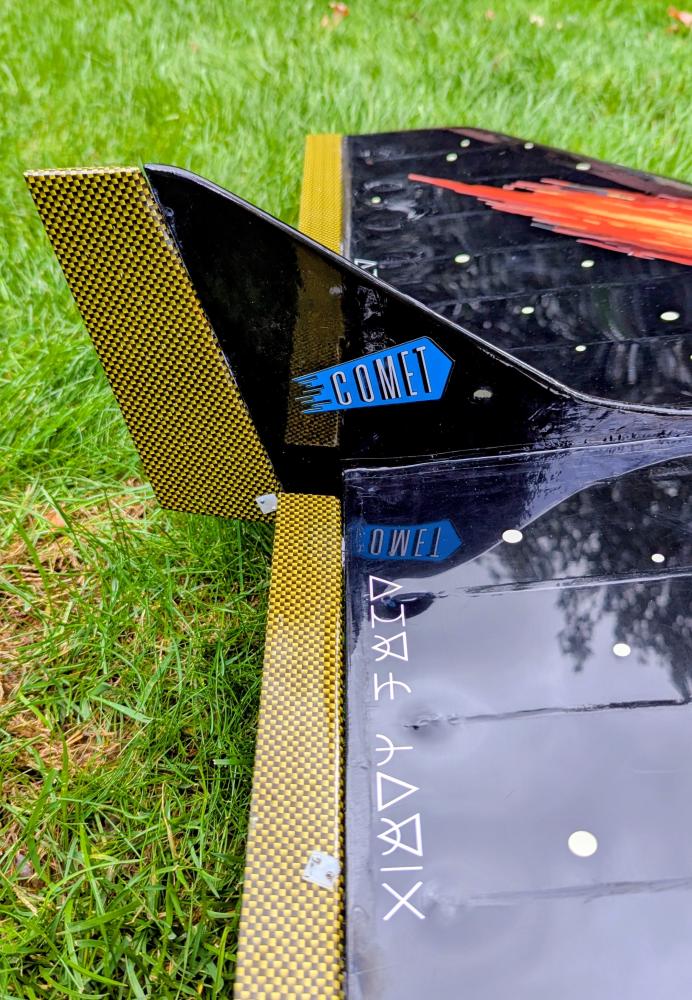 Model rocket tail fin with "Comet" branding on green grass.