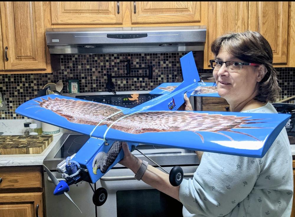 Woman holding a blue model airplane in a kitchen.