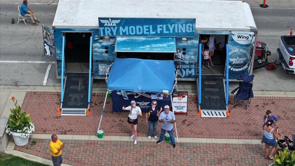 Model aviation trailer with canopy, people standing nearby on a brick path.