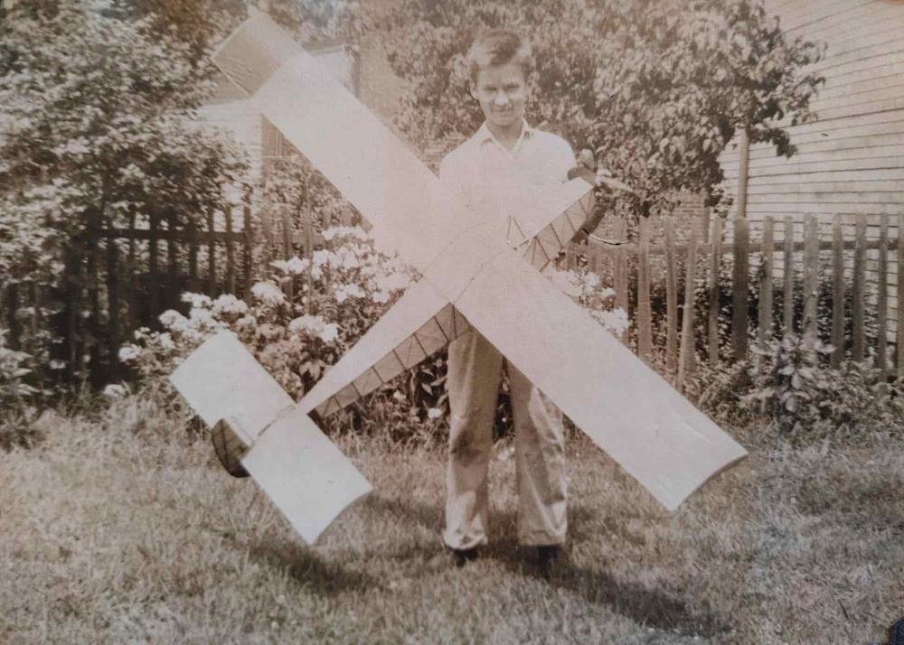 Boy holding a model airplane in a garden with a wooden fence.
