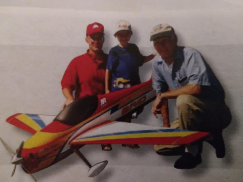 Three people with a colorful model airplane on the ground.