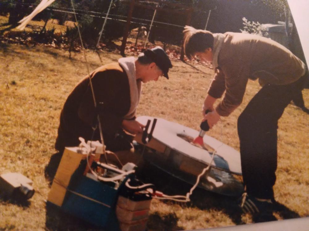 Two men assembling a satellite dish outdoors on a sunny day.