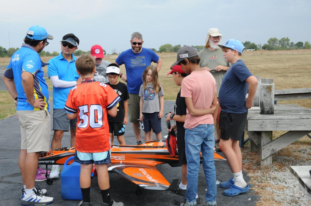 A group of people, including children and adults, gather around a large model airplane outdoors.