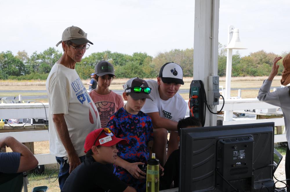People gathered around a monitor outdoors, focused on the screen.