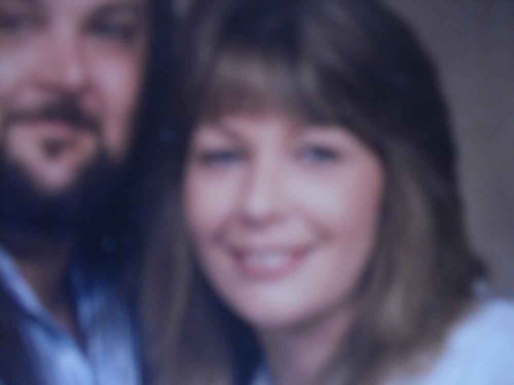 Blurry portrait of a smiling woman with medium-length hair next to a bearded man.
