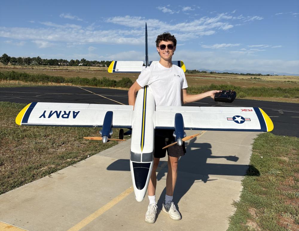 Young person holding a large model airplane on a sunny day, smiling.