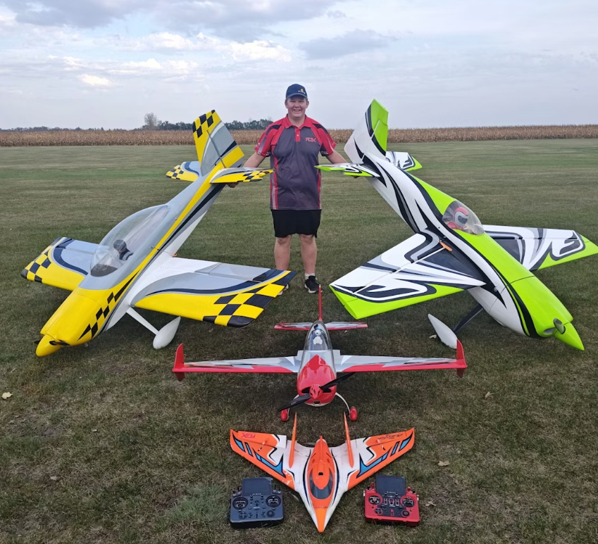 Man standing with model aircraft on grass field.