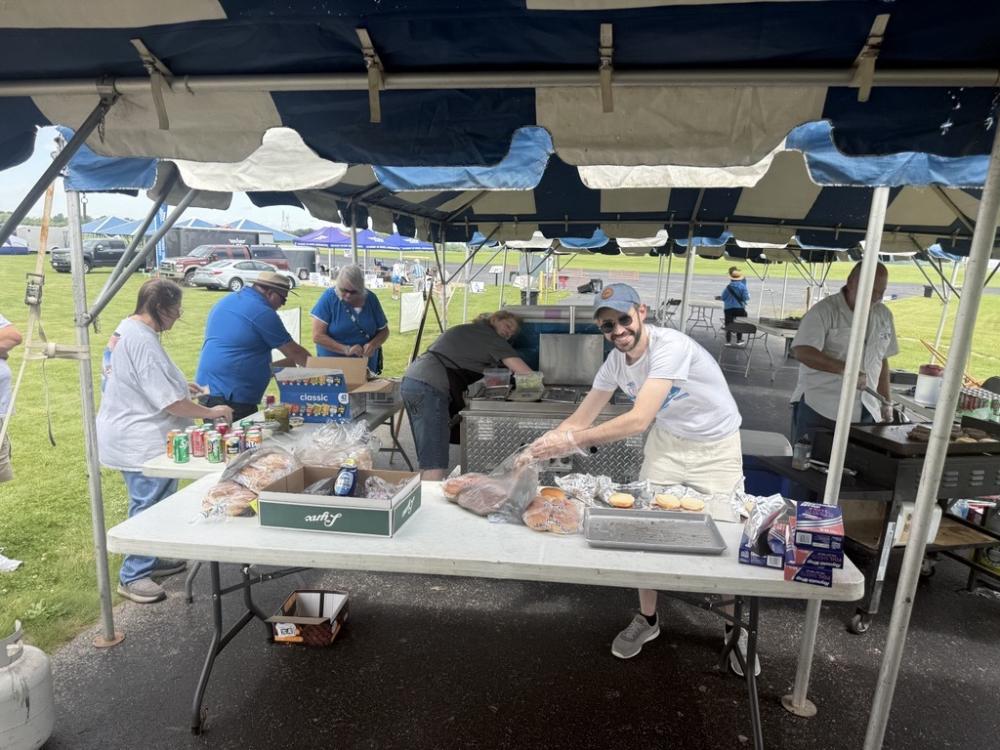 People grilling and preparing food under a blue and white tent.