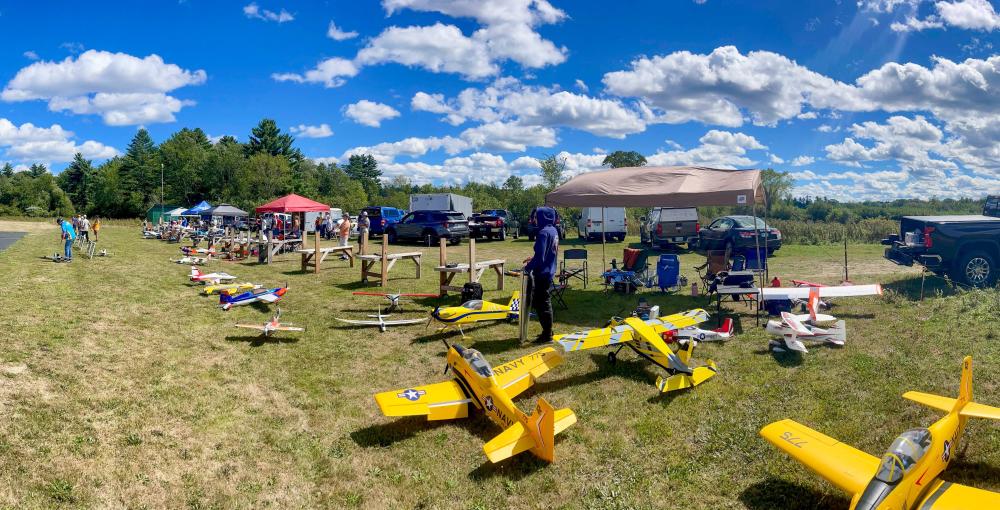 Model airplanes on grassy field with tents and trucks under a blue sky.