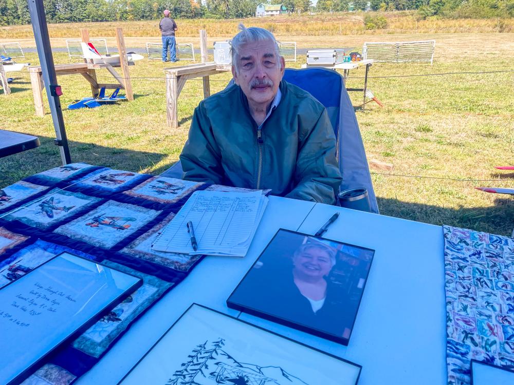 Elderly man sitting at a table with photos and documents in an outdoor setting.
