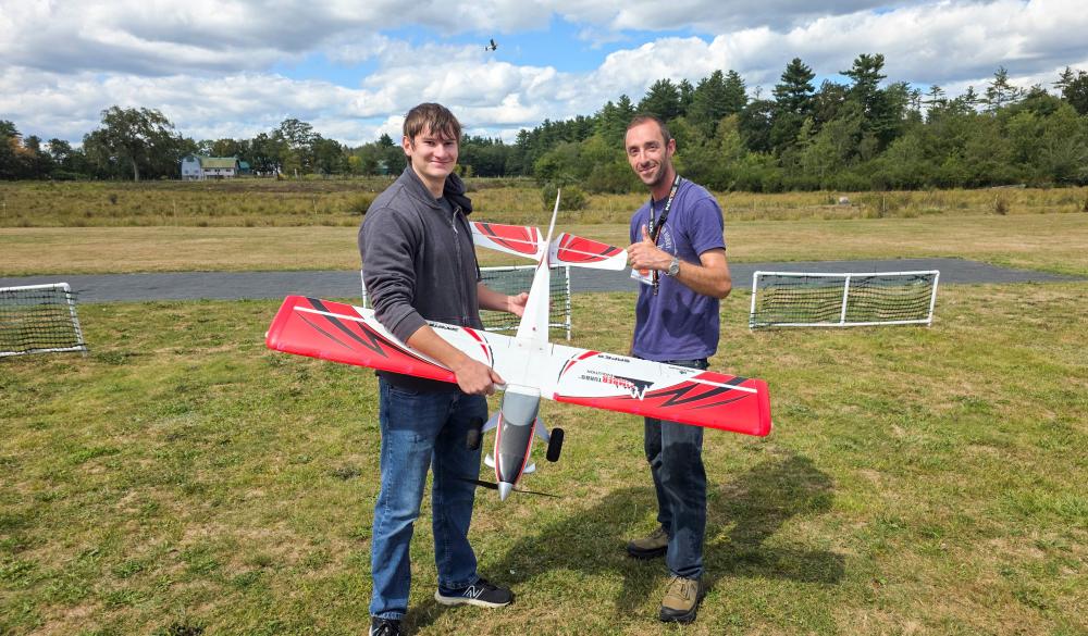 Two people holding a red and white model airplane on a grassy field.