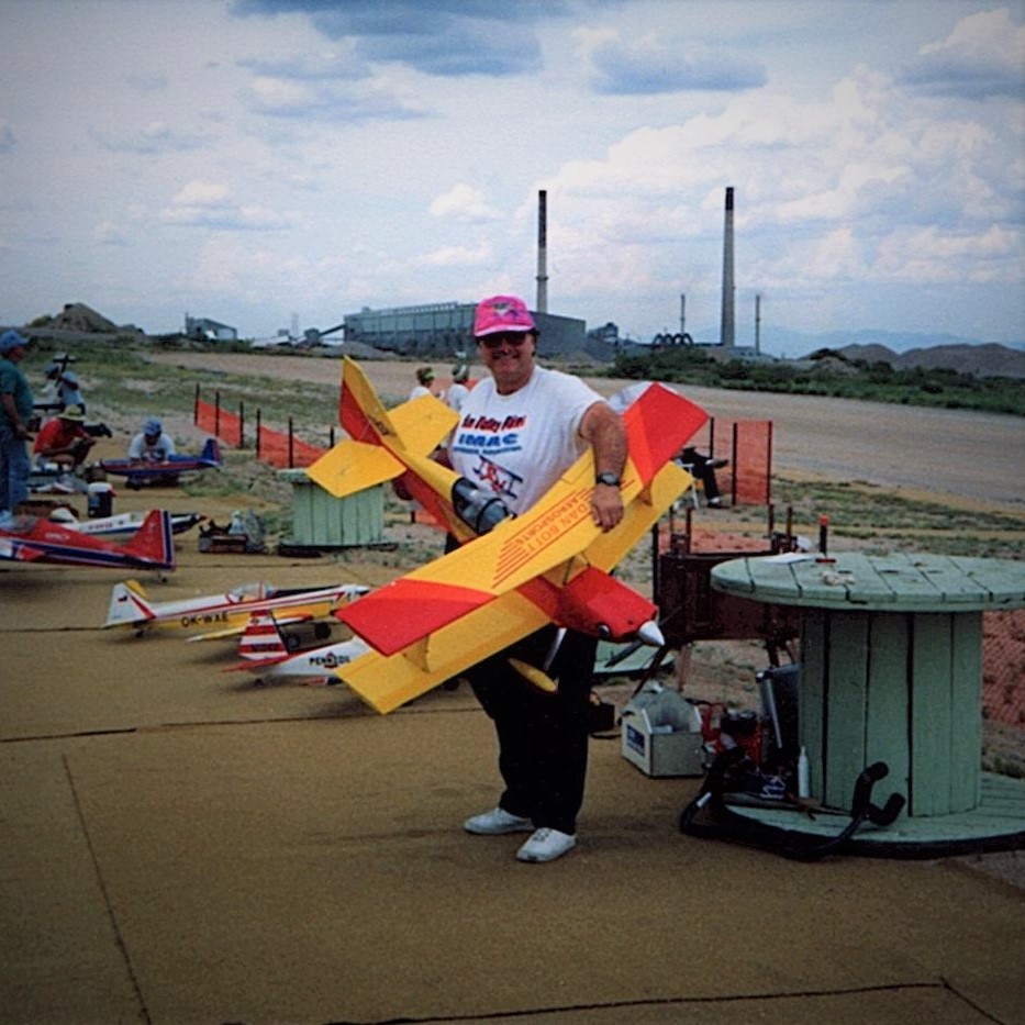 Man holding a large model airplane on an open airfield.
