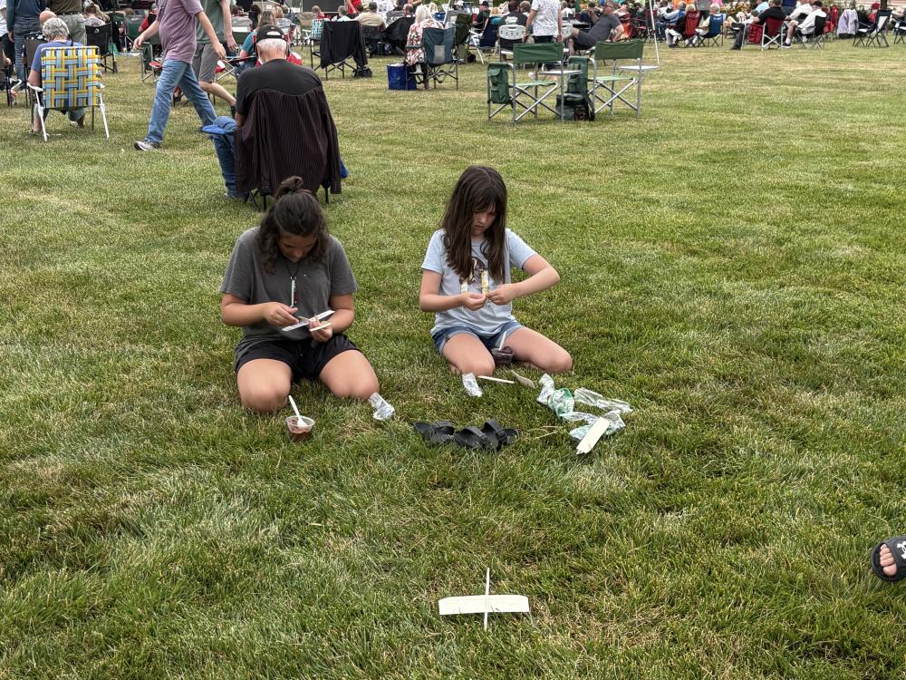 Two children sitting on grass, assembling small model airplanes.