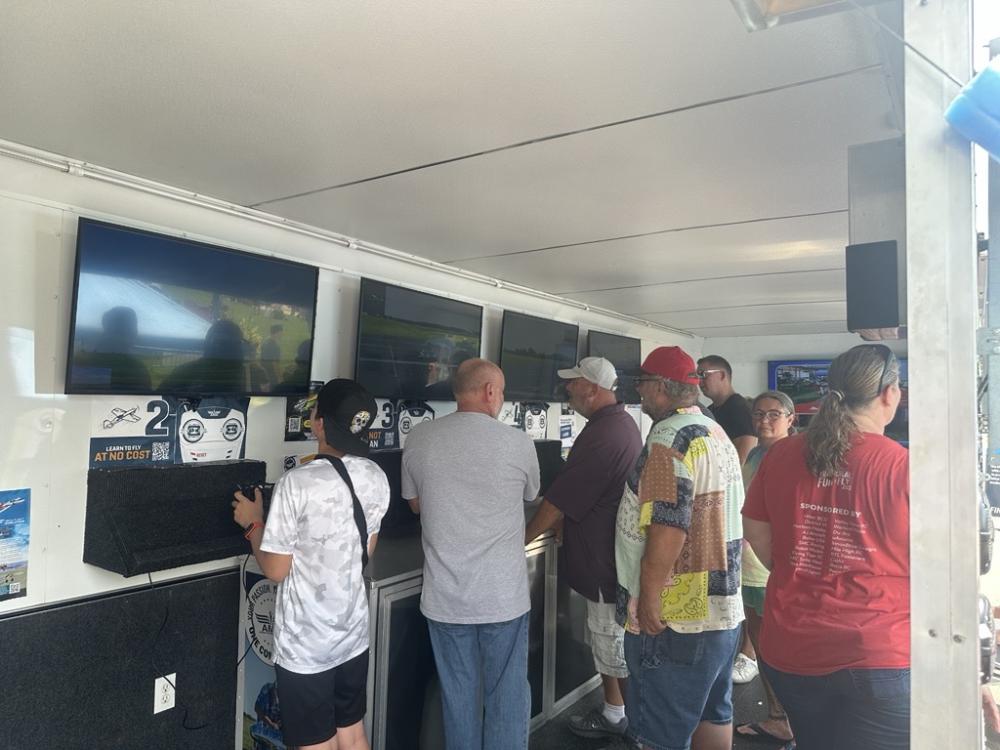 People watching screens inside a white trailer, some wearing hats.