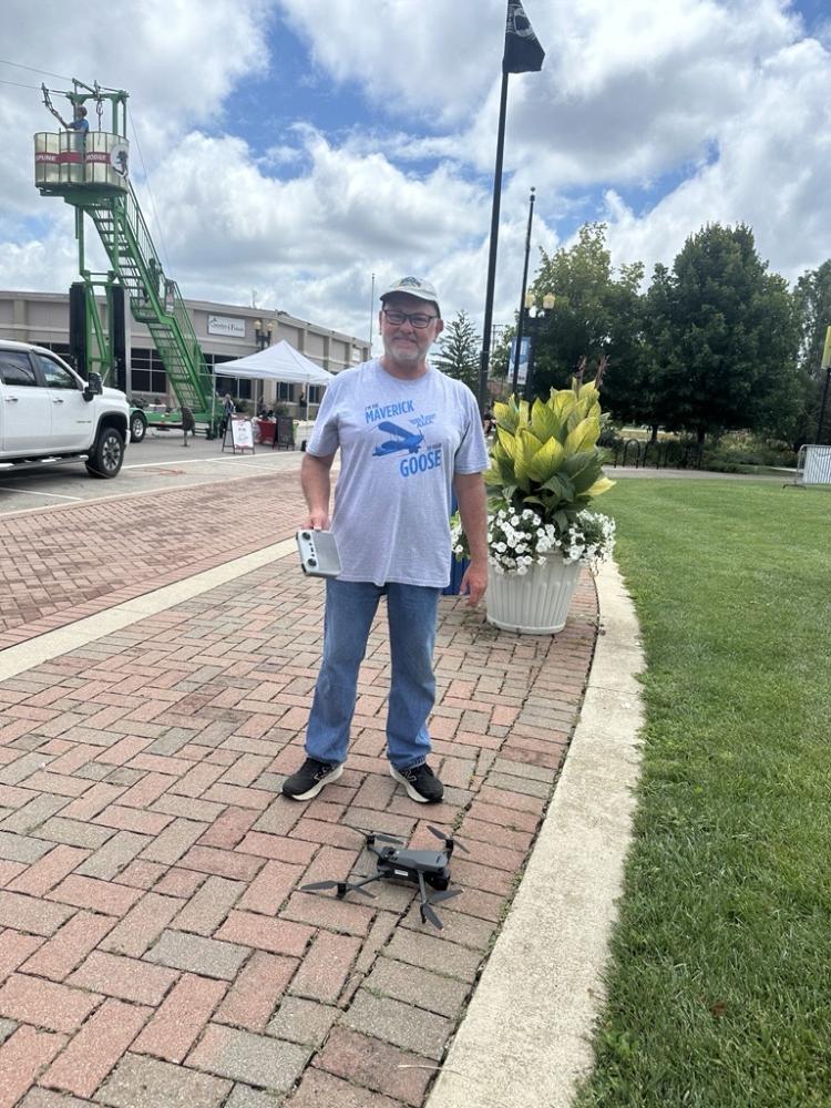 Man smiling on brick path, holding a tablet, standing near a drone.