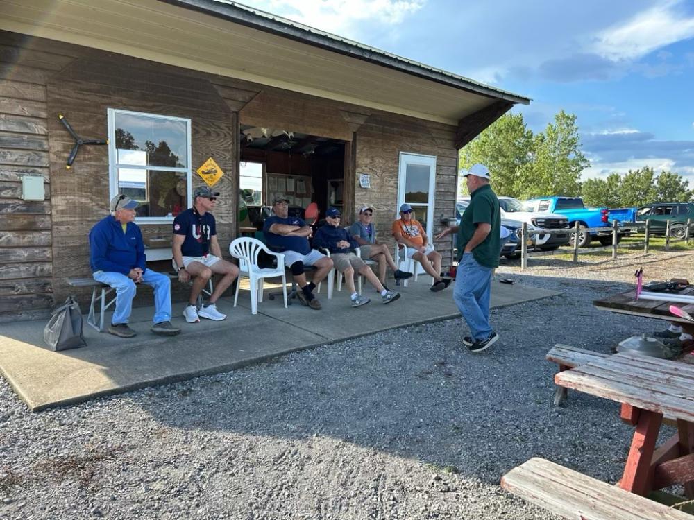 Group of men sitting and chatting outside a rustic wooden building.