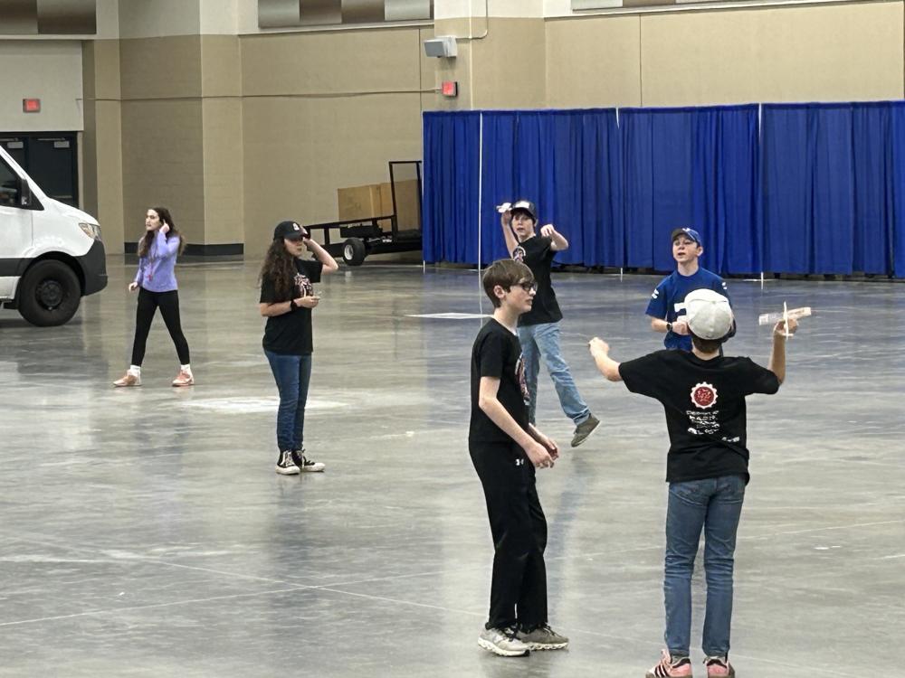 Kids flying balsa gliders in a large indoor hall.