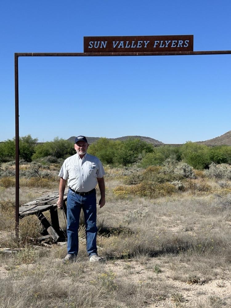 Man standing in desert under "Sun Valley Flyers" sign.