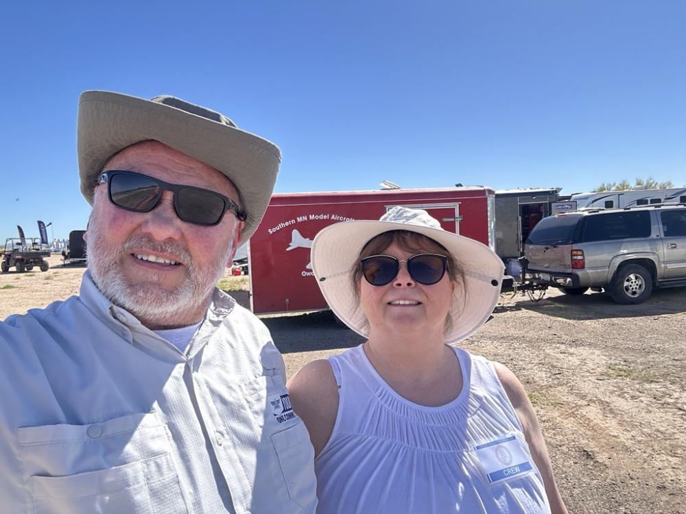 Two people wearing hats and sunglasses, standing outside on a sunny day.