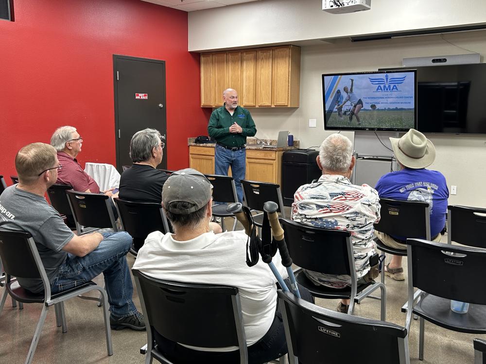 Man giving a presentation to an audience in a room with red and white walls.