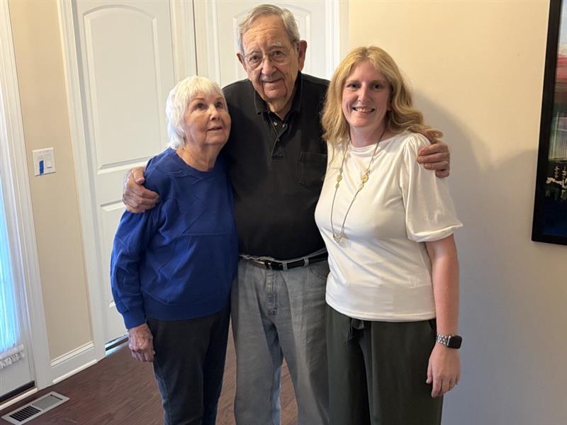 Elderly couple and young woman smiling in a hallway.